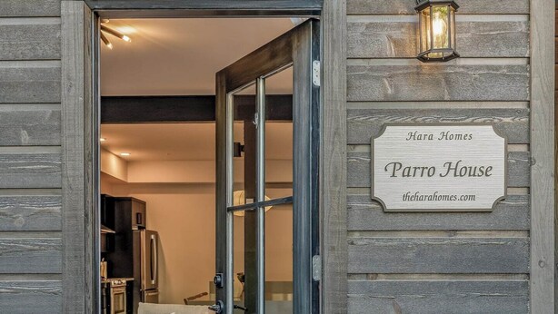 Une façade en bois avec une porte d’entrée en verre, une enseigne indiquant « Parro House », et un pot de fleurs placé à côté.