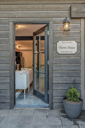 Une façade en bois avec une porte d’entrée en verre, une enseigne indiquant « Parro House », et un pot de fleurs placé à côté.