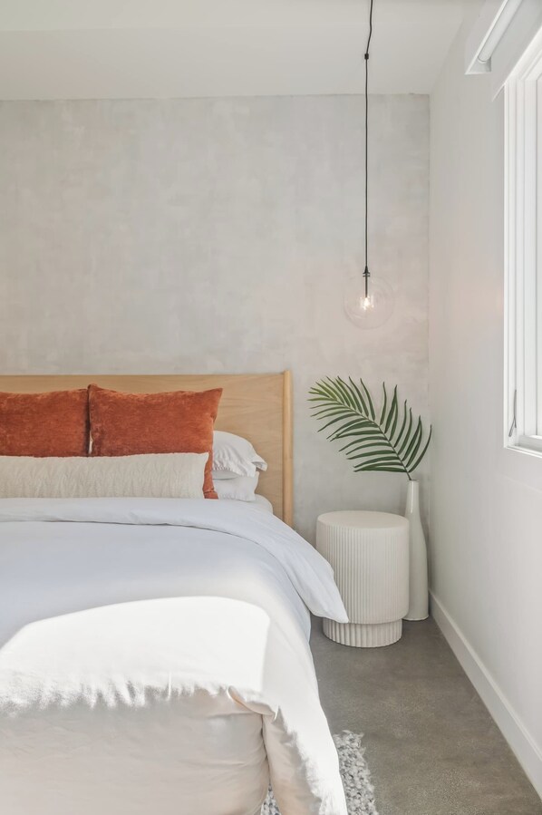Une chambre à coucher avec un lit, une plante sur la table de chevet et un luminaire suspendu.