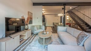 Un salon moderne avec un téléviseur à écran plat, un canapé, une table basse et un escalier.