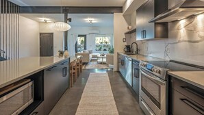 Une cuisine moderne dotée d’un îlot central, d’appareils électroménagers en acier inoxydable et d’un coin repas comprenant un canapé et une table.