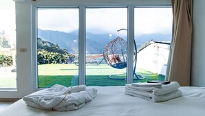 Een hotelkamer met een bed, een hangstoel en uitzicht op bergen door grote ramen.