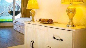Een hotelkamer met een bed, twee lampen, een schaal met snacks en uitzicht op bergen door een raam.