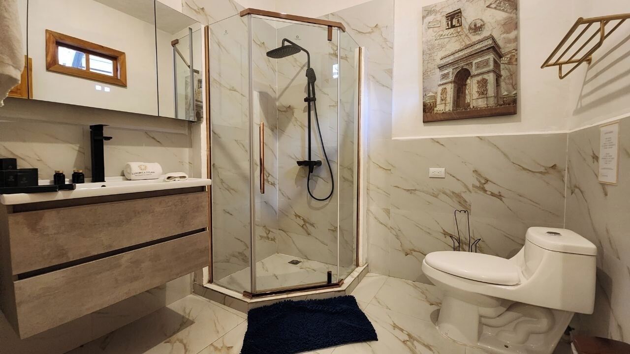 A bathroom with a glass-enclosed shower, a white toilet, and a marble floor.
