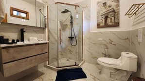 Et badeværelse med en brusekabine med glasvægge, et hvidt toilet og en marmorgulv.