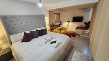 A hotel room with a large bed, a desk, a chair, a TV, and a small table with a plant.