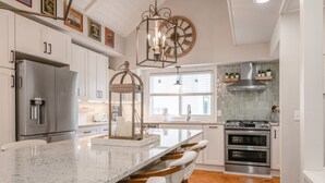 A kitchen with a large island, stainless steel appliances, and a decorative clock. - Goin' Coastal: East Beach 5BR Retreat | Private Pool | Steps to Beach | Sleeps 12 (Saint Simons Island)