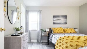 A bedroom with a bed, bedside table, lamp, and a window with curtains.