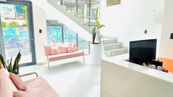Ein moderner Empfangsbereich mit einem rosafarbenen Sofa, einem Empfangstresen, einer Treppe und einem großen Fenster mit Blick.
