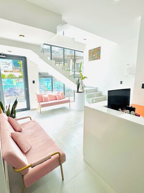 A modern reception area with a pink sofa, a reception desk, a staircase, and a large window with a view. - TIBERIAS by luxury atitlan (San pedro la Laguna solola)