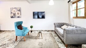 A living room with a blue armchair, grey sofa, patterned rug, small table, and a hanging light fixture.