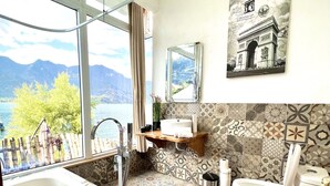 A bathroom with a bathtub, toilet, and sink, featuring patterned tiles and a view of mountains through large windows.