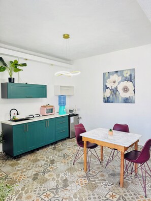 A modern kitchen with teal cabinets, a white countertop, and a patterned tile floor.