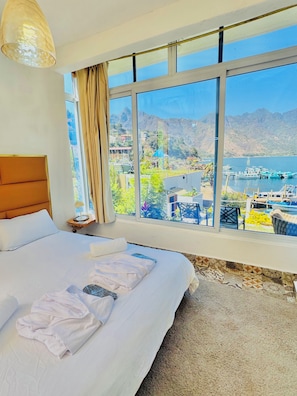 Een hotelkamer met een groot bed, uitzicht op een bergachtig landschap en een wateroppervlak.