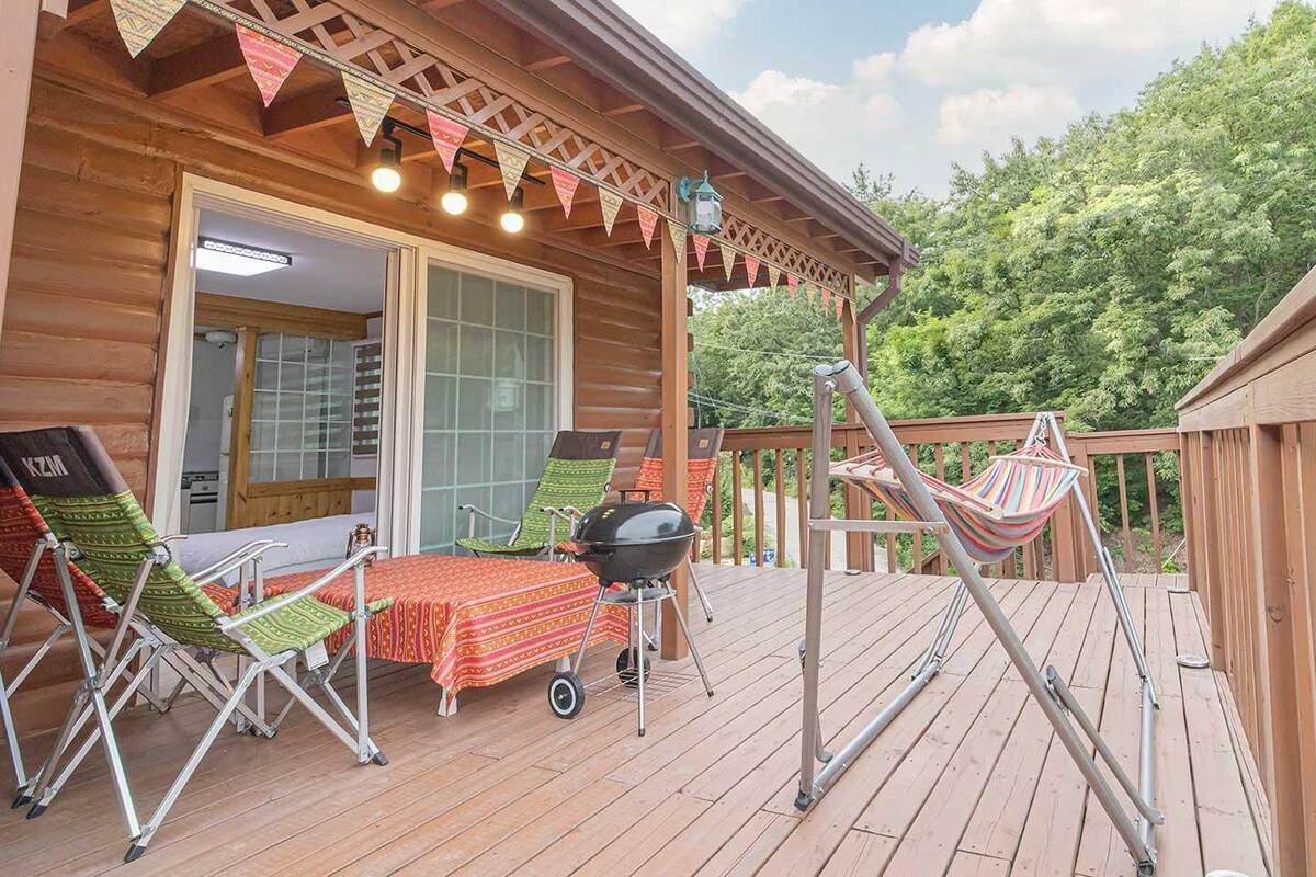 A wooden cabin with a deck, outdoor seating, a grill, and a hammock.