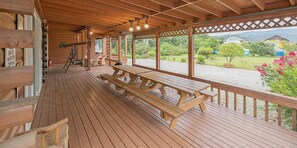 Una terraza de madera con mesas de picnic y vistas a un paisaje verde.