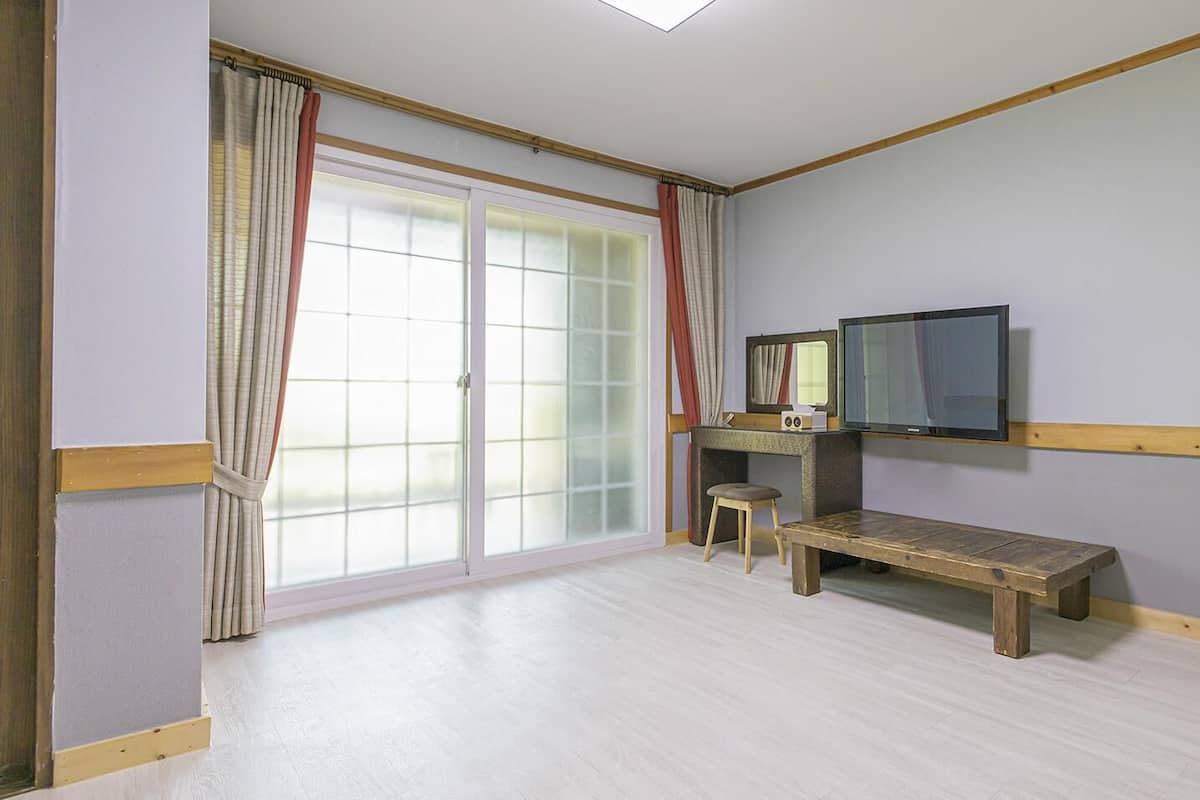 A room with a sliding glass door, a bench, a small stool, and a television mounted on the wall.