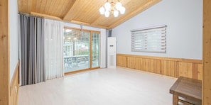 Une pièce spacieuse avec un plafond en bois, une grande porte-fenêtre coulissante donnant sur un espace extérieur, un climatiseur blanc et un banc en bois.