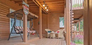 Una cabaña de madera con un porche que tiene dos sillas de mimbre, una mecedora y una mesita con un cojín azul.