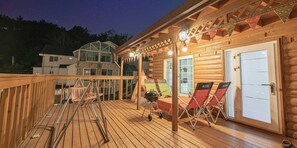 Terraza de madera con cerramiento de vidrio, mobiliario exterior y una parrilla de barbacoa.