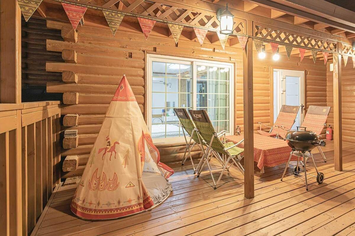 A log cabin with a wooden deck, a covered seating area, and a grill.