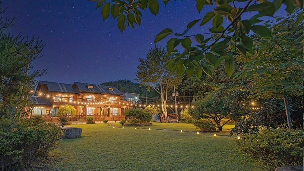 A large, two-story wooden house with a balcony, surrounded by a well-maintained lawn and trees. - Gyeongju Cabinhouse (Gyeongju)