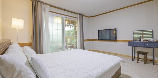 Habitación de hotel con una cama grande, un escritorio con silla, un televisor y una ventana con cortinas.