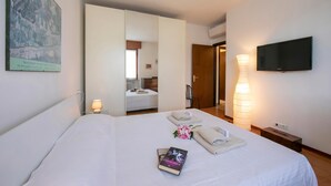 A hotel room with a bed, a TV, a bedside lamp, a painting, and a bathroom visible through an open door. - Casa di Paola: Lake-View Balcony Apartment in Peschiera, Peschiera del Garda, Italy (Peschiera del Garda)