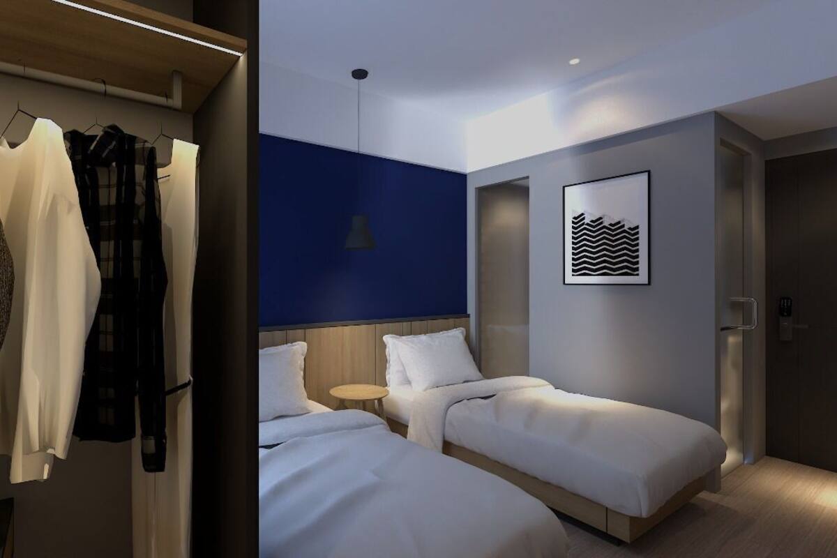 A hotel room with two beds, a wardrobe, a small round table, and a wall-mounted artwork.