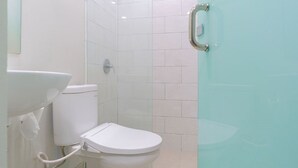 A bathroom with a white toilet, a sink, and a glass shower enclosure. - LeGreen Suite Sudirman (Jakarta)