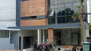 A modern building with a mix of brick and glass facade, a covered entrance, and parked motorcycles. - LeGreen Suite Sudirman (Jakarta)