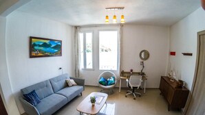 A living room with a sofa, a coffee table, a desk, and a chair. There is a painting on the wall, a window with curtains, and a ceiling light fixture. - San Pedro Suite (San pedro la Laguna solola)