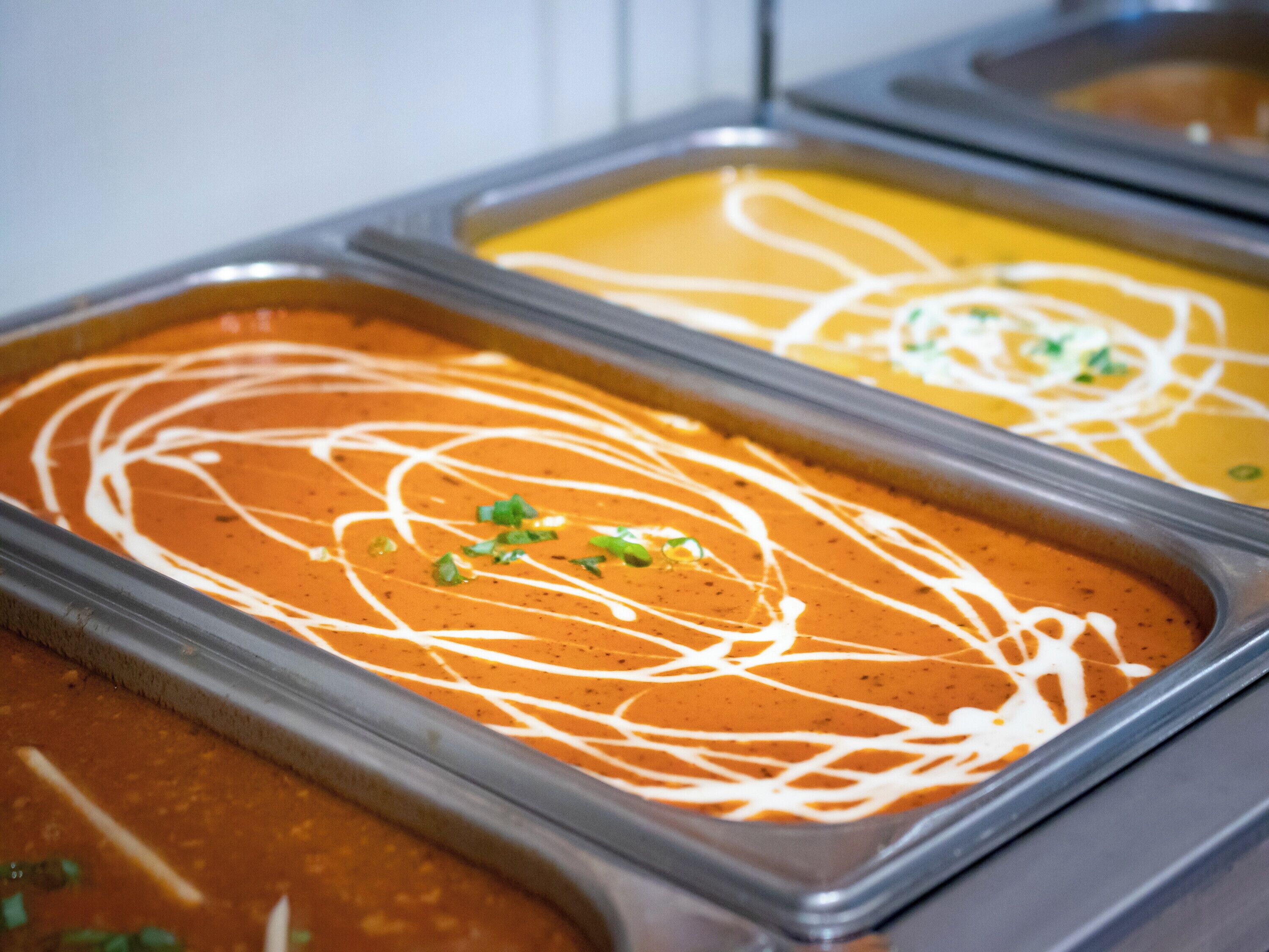 A buffet with various dishes, including a red sauce with white drizzle and garnishes, a yellow dish, and a brown dish.