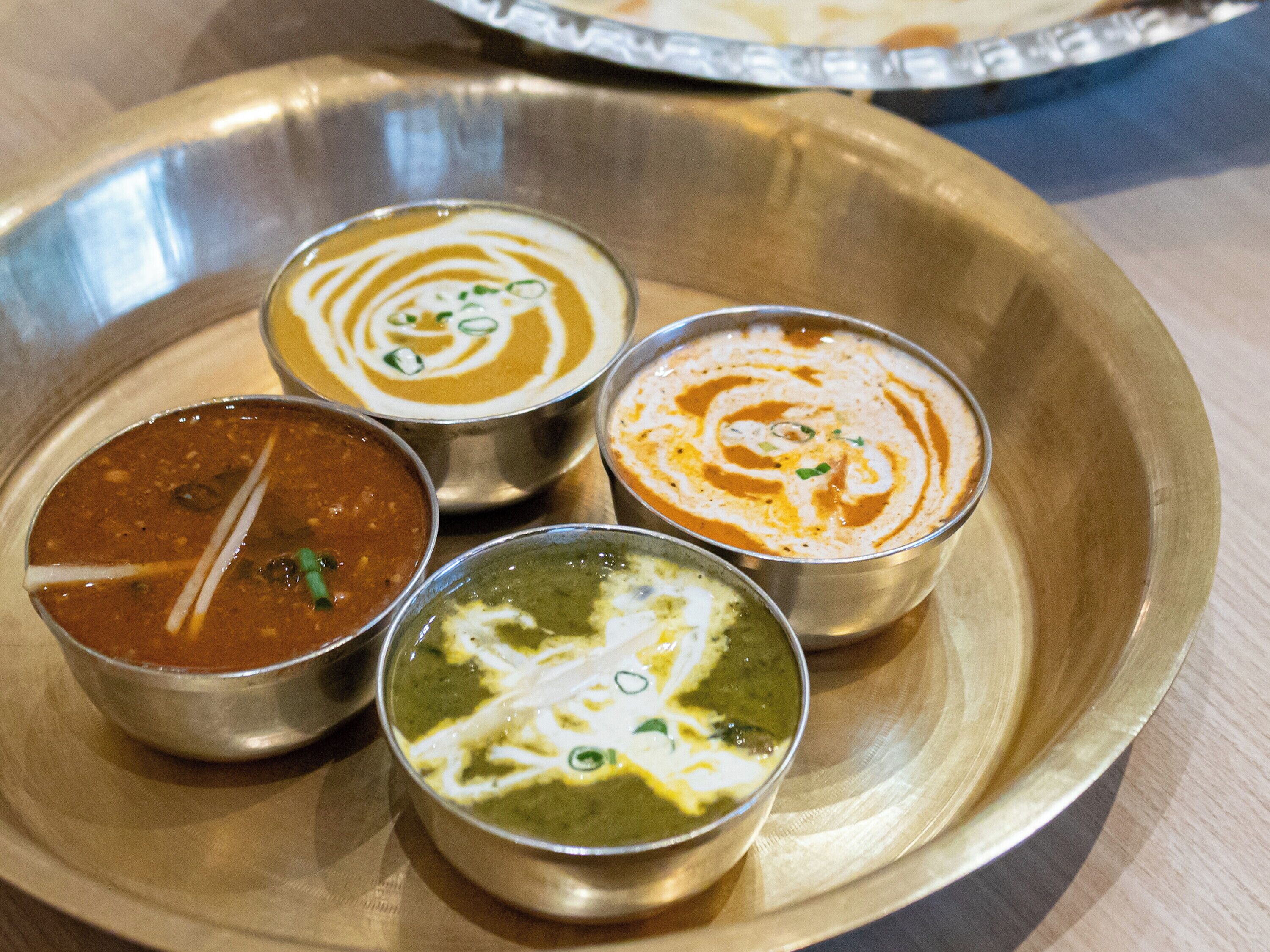 Cuatro recipientes metálicos con salsas de colores diferentes sobre una bandeja de metal.