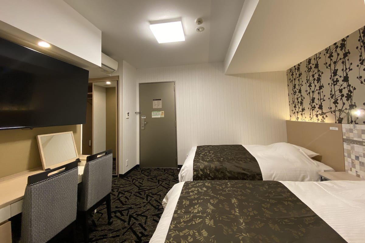 Een hotelkamer met twee bedden, een bureau met stoel, een flatscreen televisie en een deur naar een andere kamer.