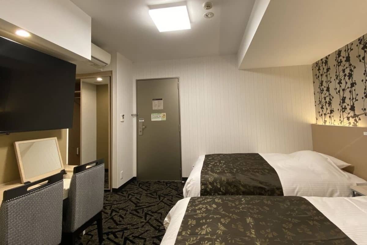 Een hotelkamer met twee bedden, een bureau met stoel, een flatscreen televisie en een deur die uitkomt op een gang.