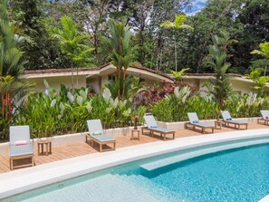 Zona junto a la piscina con sillones de descanso y una piscina, rodeada de exuberante vegetación tropical.