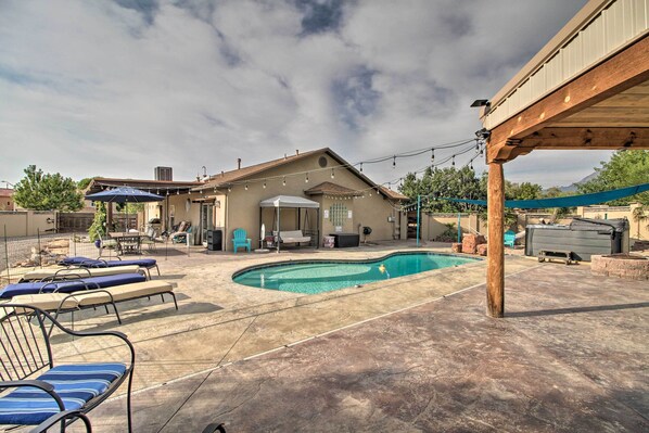 A backyard with a swimming pool, lounge chairs, and a covered patio area.