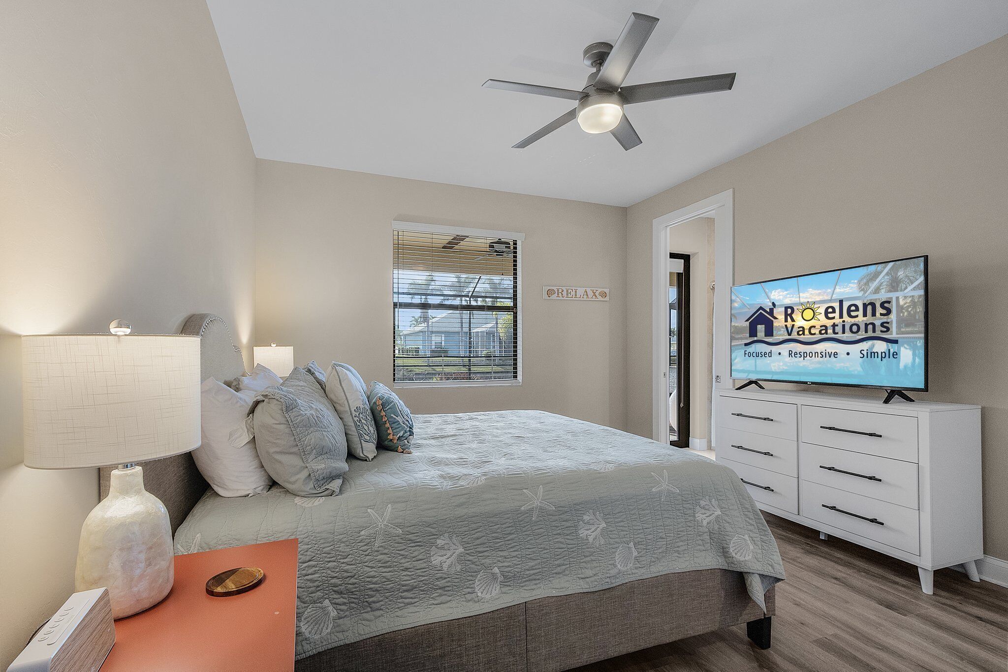 A bedroom with a bed, a TV, a ceiling fan, a nightstand, and a window with blinds.