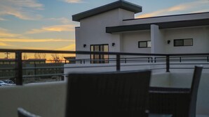 Ein modernes Gebäude mit flachem Dach und großen Fenstern, betrachtet von einem Balkon mit Sitzgelegenheiten.