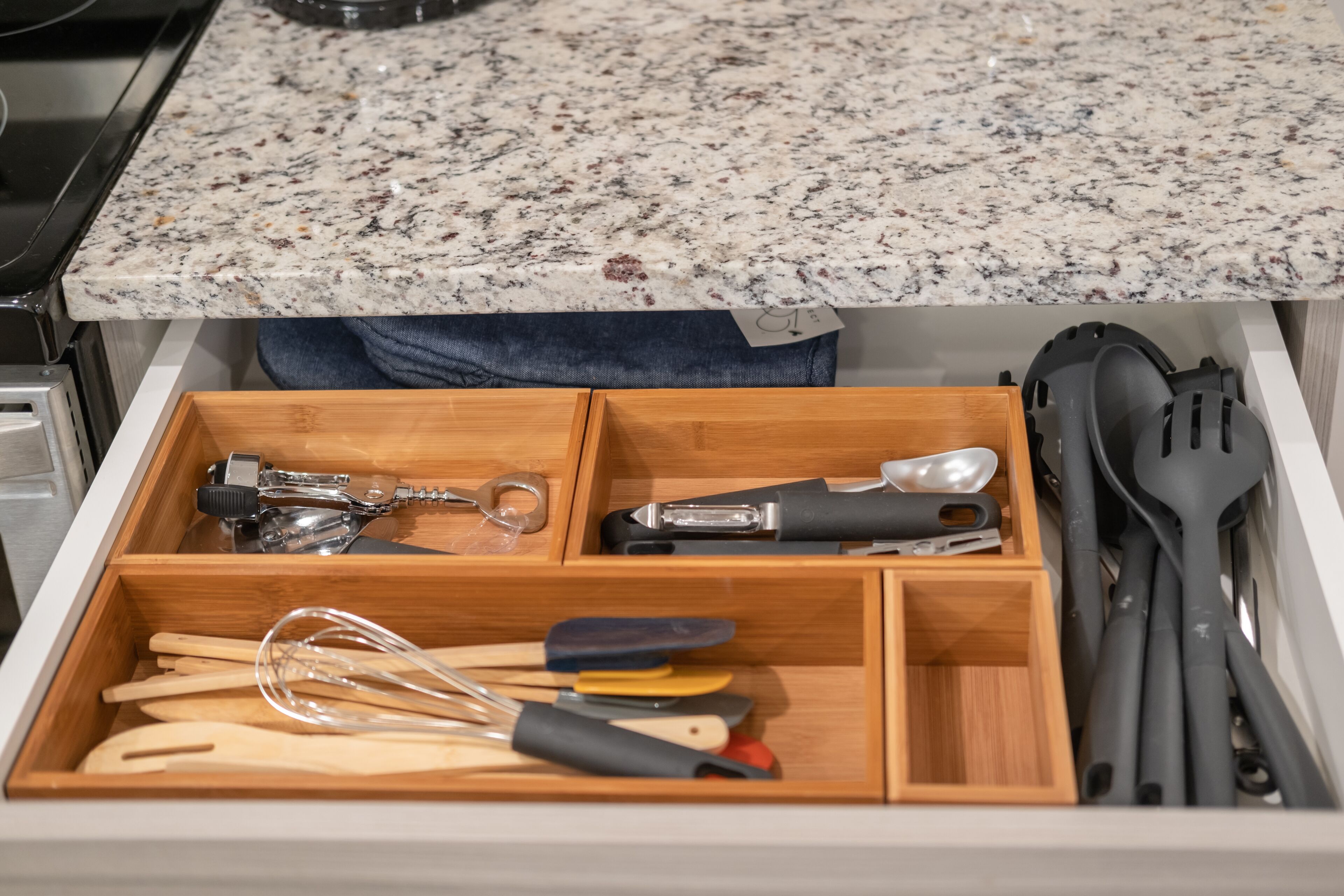 Un tiroir de cuisine contenant des ustensiles en bois, une râpe et une spatule.