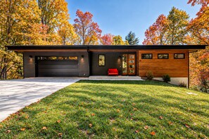 Une maison moderne à deux étages, dotée d’un garage, d’un banc rouge et d’une pelouse bien entretenue.