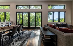 Un salon moderne avec un coin repas, de grandes fenêtres et une vue sur les arbres.
