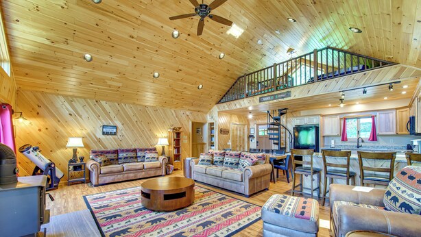 A spacious living area with a high ceiling, a fireplace, a large round coffee table, and a cozy seating arrangement.