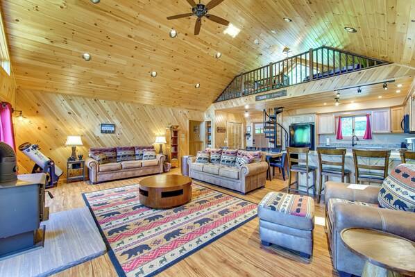 A spacious living area with a high ceiling, a fireplace, a large round coffee table, and a cozy seating arrangement. - 'Adirondack Dream' Your Lakefront Escape (Black Brook)