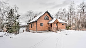 Eine Blockhütte mit einem steilen Dach, einer Veranda und einer verschneiten Landschaft.
