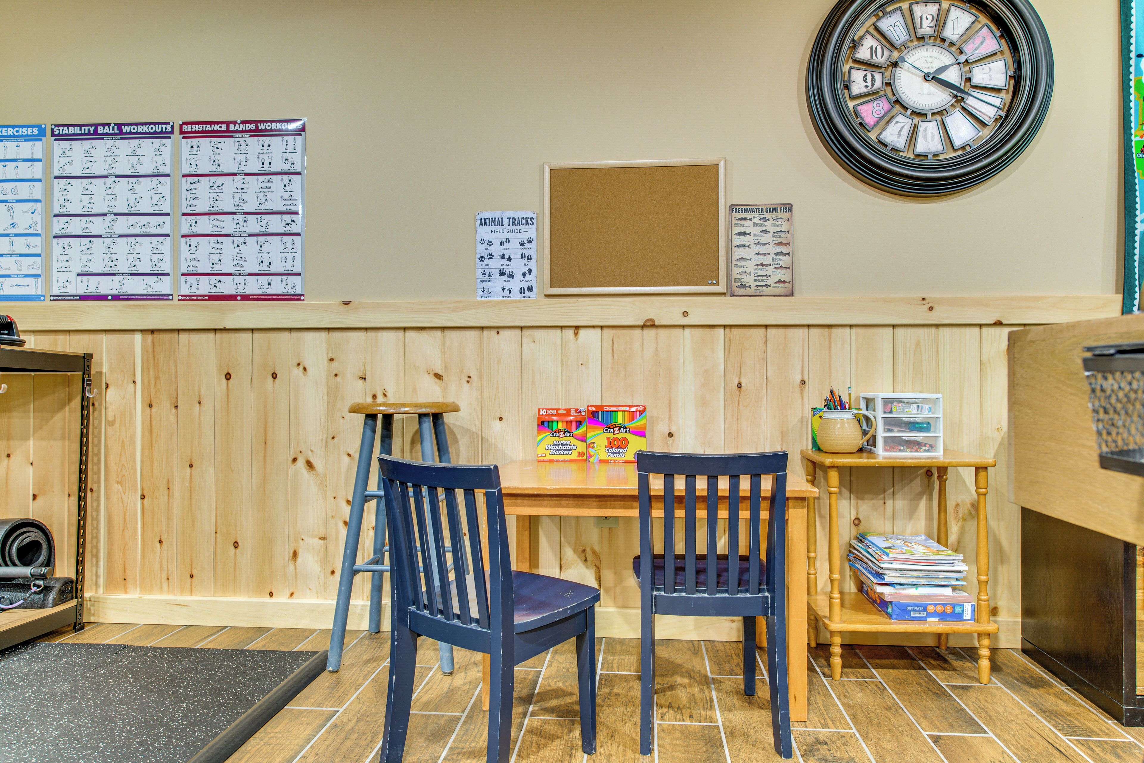 A room with two blue chairs, a wooden table, a wall clock, and various educational posters.