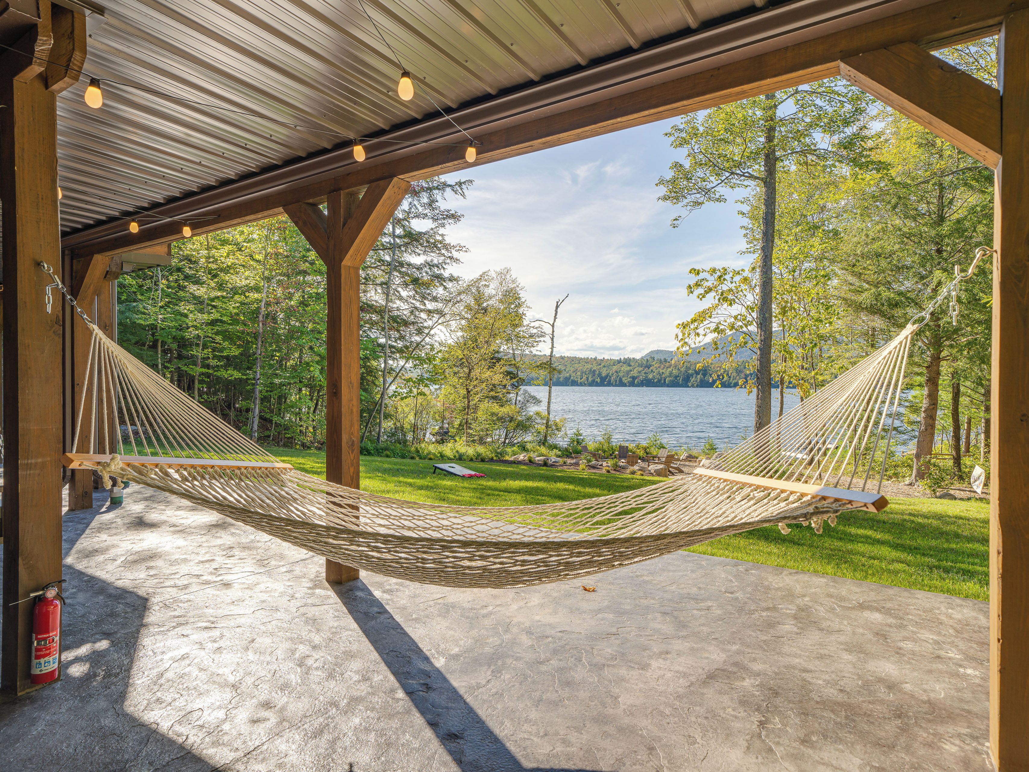 A hammock under a wooden structure with a view of a lake and trees.