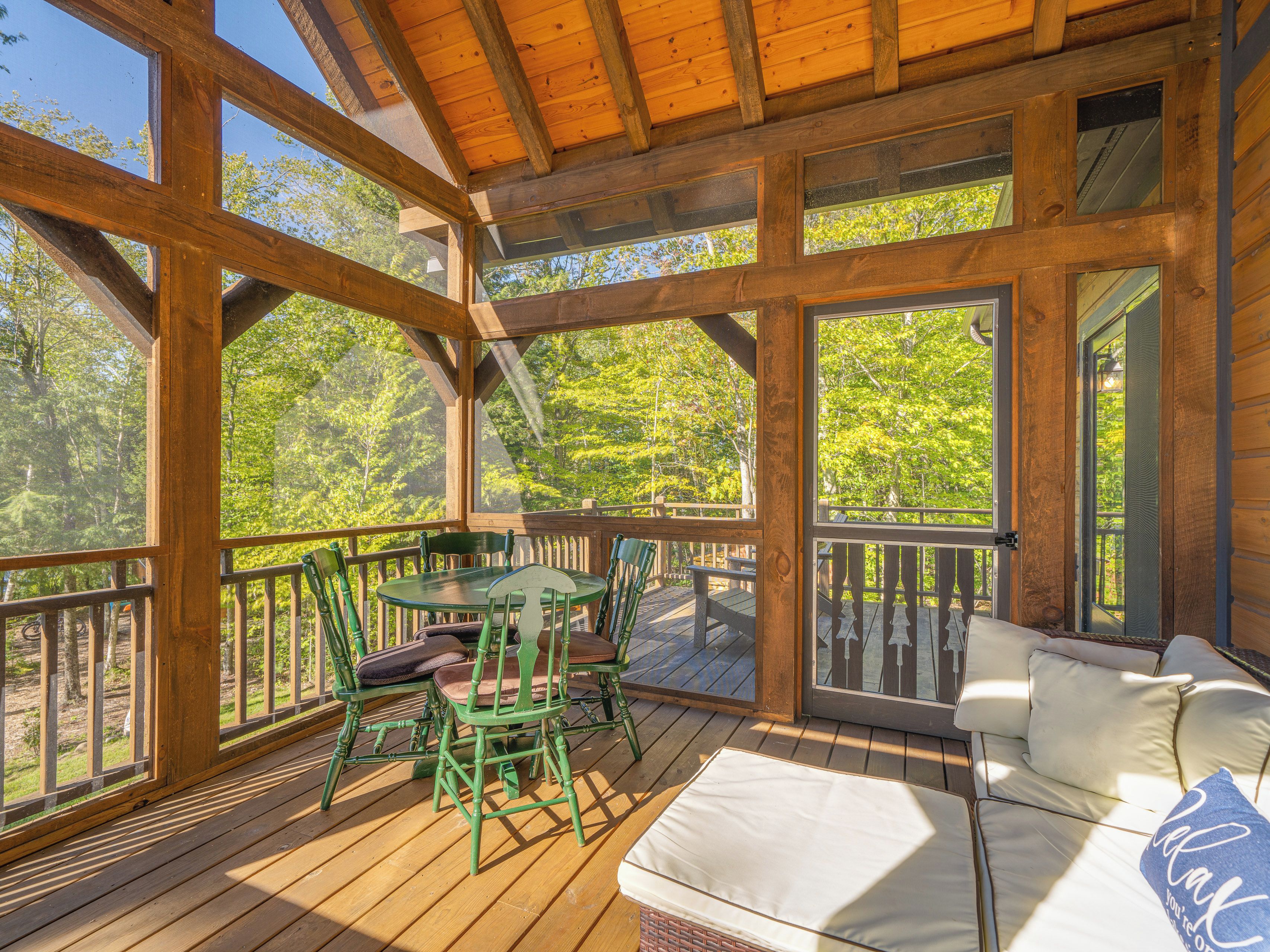 Eine Holzterrasse mit Tisch, Stühlen und einer Couch, mit Blick auf Bäume.