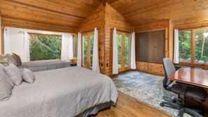 Une chambre confortable dans un chalet, avec un lit, un bureau et de grandes fenêtres donnant sur la forêt.